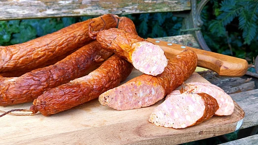 Uzené klobásy na dřevěném prknu s nůžkou vedle.