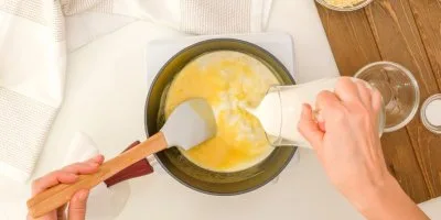 Ruce nalévají mléko do mísy s vejci na dřevěném povrchu.