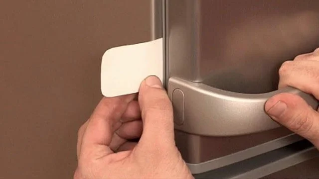 Ruce opravují těsnění dveří ledničky lepicí páskou.