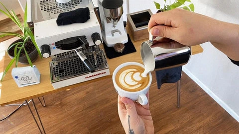 Člověk nalévá mléko do kávy pro vytvoření latte artu.