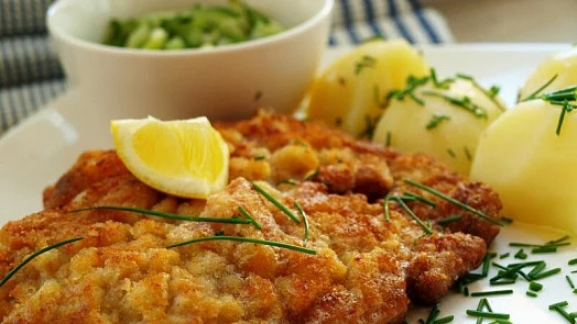 Zlatavý řízek s bramborami, citronem a petrželkou na talíři.