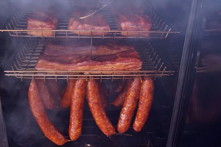 Uzená klobása a maso v kouři na grilu.