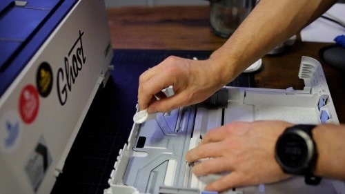 Ruční čištění vnitřních částí bílé tiskárny na pracovní ploše.