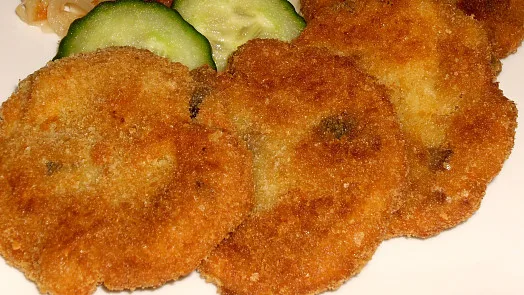 Zlatohnědé obložené řízky s kouskem okurky na bílém talíři.