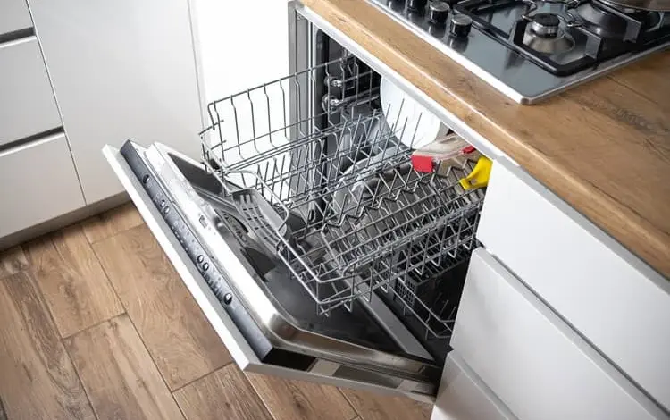 Otevřená myčka s nádobím u dřevěné pracovní desky.