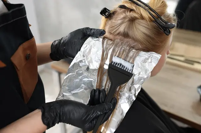 Stylista aplikuje barvu na vlasy pomocí štětce.