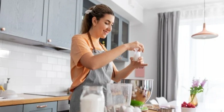 Žena vaří v kuchyni, přidává ingredience do mísy.