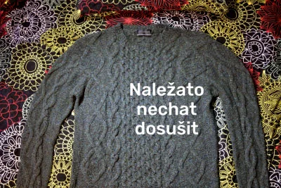 Šedý vlněný svetr položený na barevném vzorovaném podkladu.