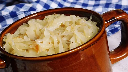 Uvařené kysané zelí v hnědém hrnku na pruhovaném ubrusu.