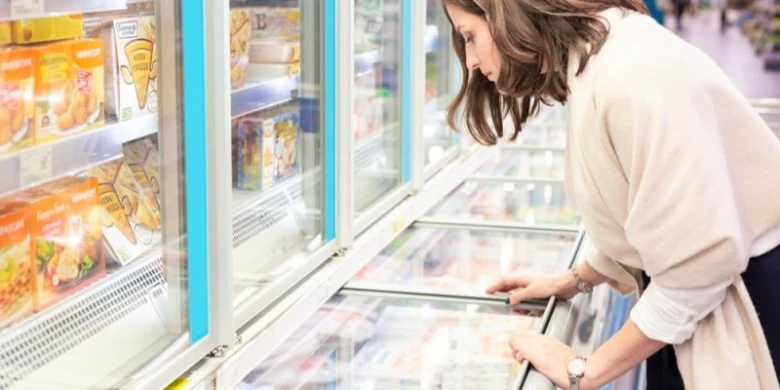 Žena kontroluje mražené potraviny v supermarketu.