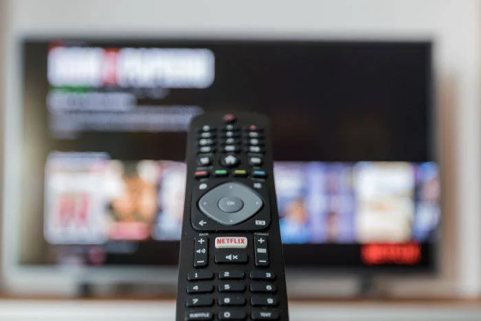 Černé dálkové ovládání před televizorem s rozostřeným obrazem.