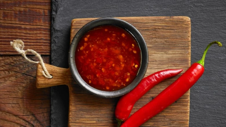 Červené chilli papričky vedle misky s omáčkou na dřevěném prknu.