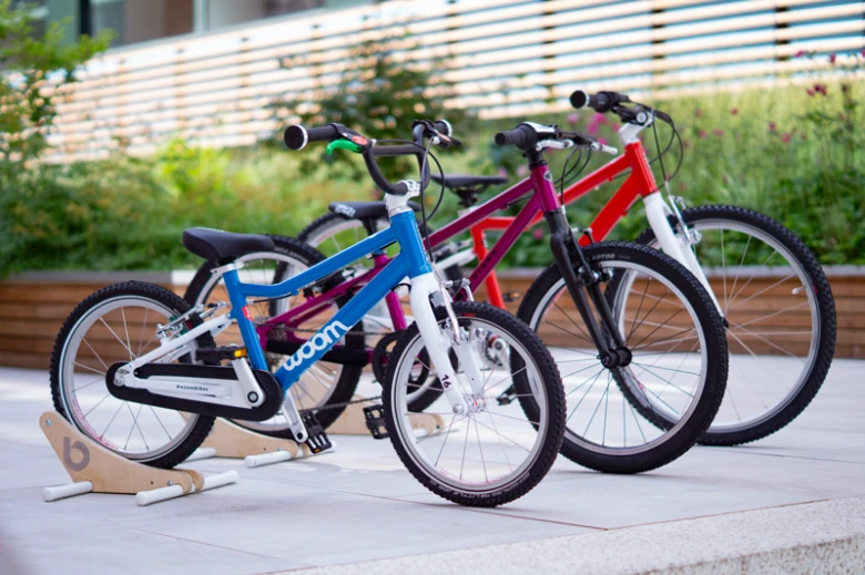 Tři barevné dětské bicykly stojící vedle sebe venku.