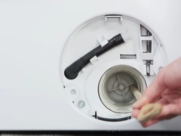 Ruční čištění filtru pračky při údržbě.