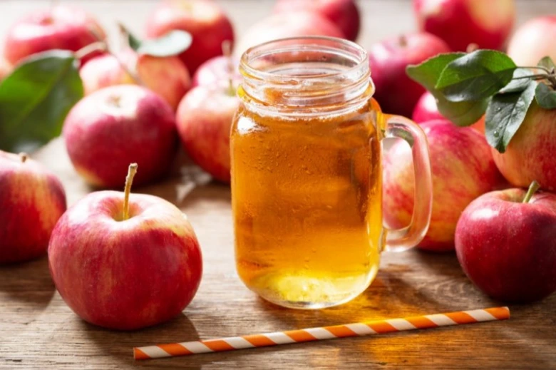 Sklenice jablečného octu s medem obklopená čerstvými jablky.