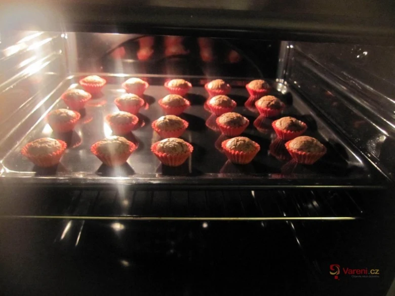 Muffiny se pečou v troubě na plechu s červenými papírovkami.