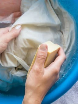 Ruční praní oblečení mýdlem v modré míse s bublinkami.