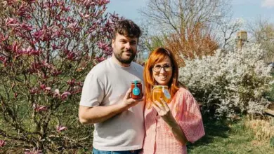 Muž a žena drží sklenice medu v zahradě s kvetoucími stromy.