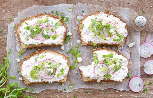 Čtyři toasty s krémovým sýrem a ozdobou z ředkviček.