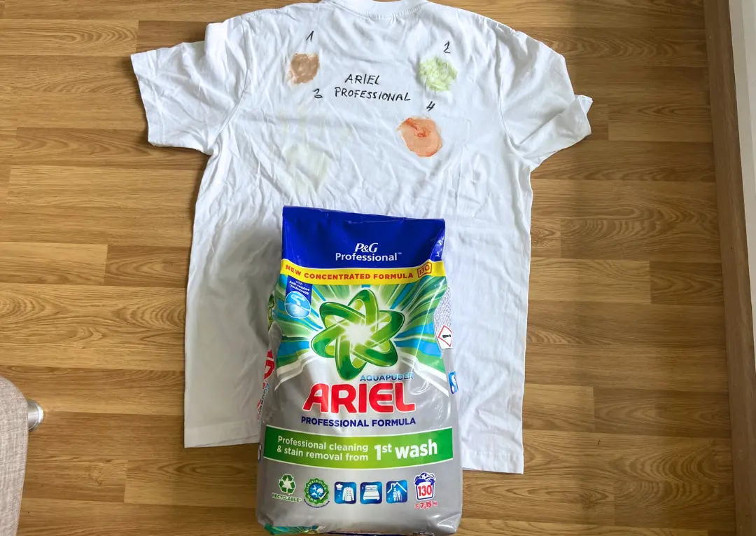 Bílá košile s fleky vedle pracího prášku Ariel