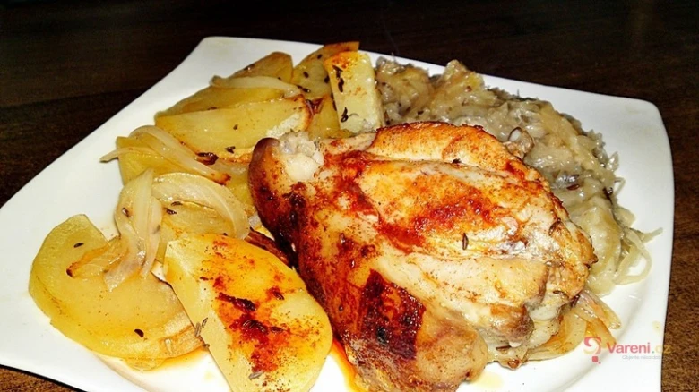 Pečené kuřecí koleno s bramborami a zelím na bílém talíři.