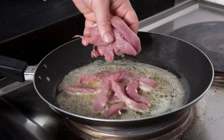 Ruce kladou surové vepřové maso do horké pánve.