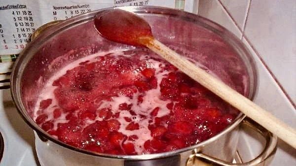 Kuchta v hrnci s vařící se jahodovou marmeládou a pěnou.