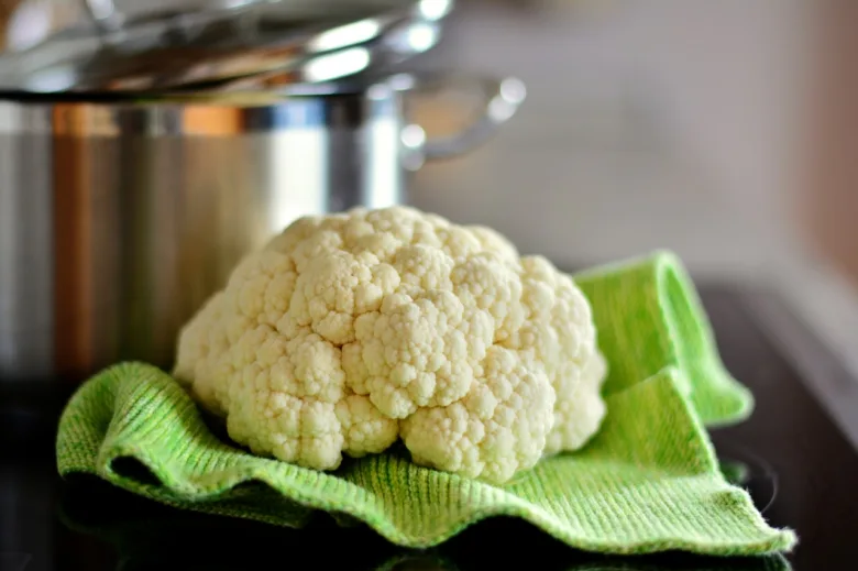 Čerstvý květák na zelené utěrce před hrncem.