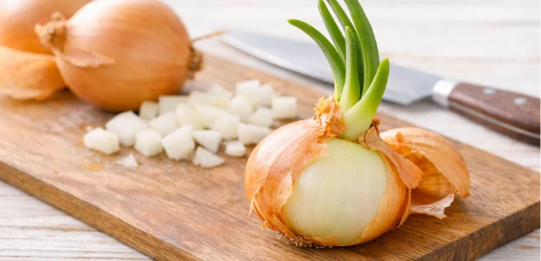 Cibule celá i nakrájená na dřevěném prkénku s nožem.
