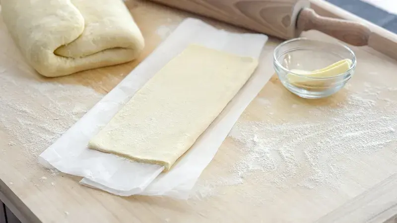 Listové těsto rozválené na papíře s máslem vedle válcovky.