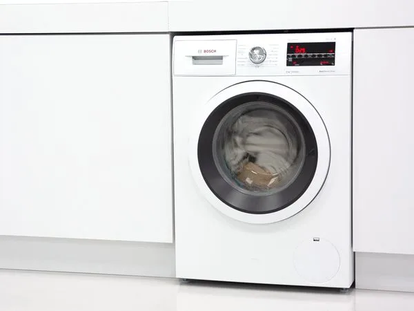Bosch pračka s oblečením uvnitř mezi kuchyňskými skříni.