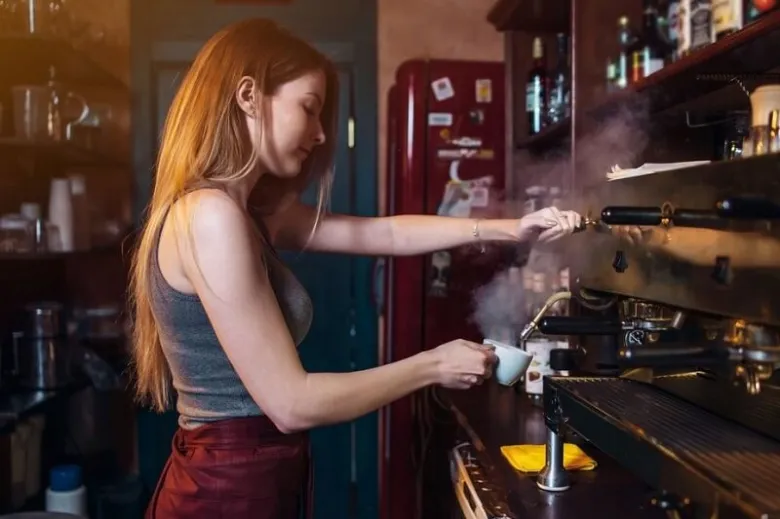 Baristka připravuje espressa v kávovaru s tlakem.