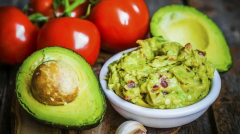 Čerstvé avokádo, rajčata a domácí guacamole na dřevěném povrchu.