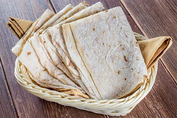Koš s vrstvenými plackami chleba lavash na dřevěném stole.