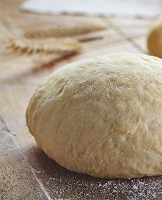 Kulová kouska těsta na dřevěném prknu s moukou.