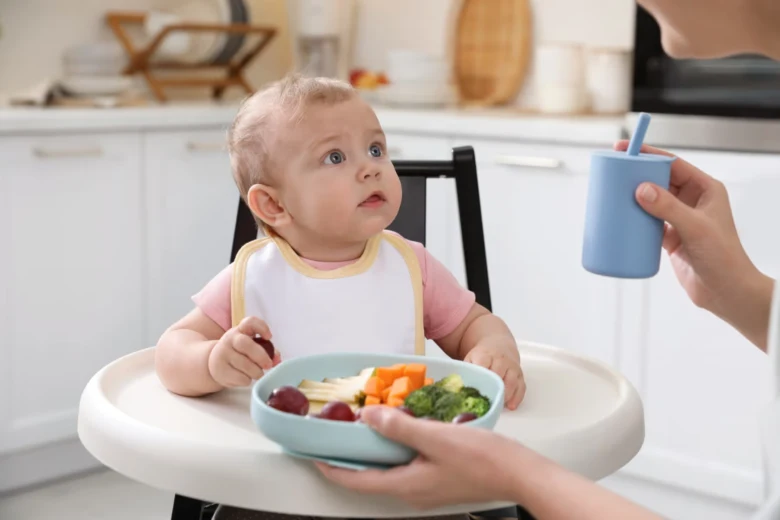 Dítě v jídelní židli s ovocem a zeleninou na talíři.