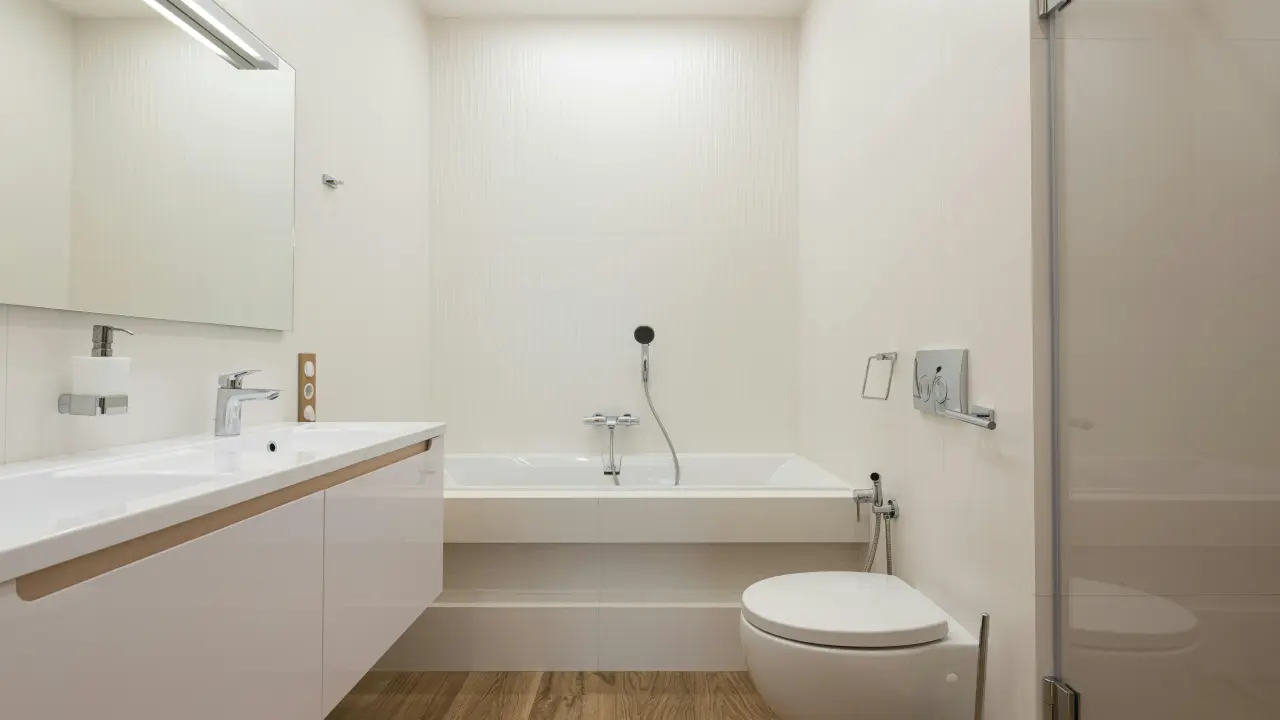 Moderní koupelna s bílou vanou a toaletou na dřevěné podlaze.