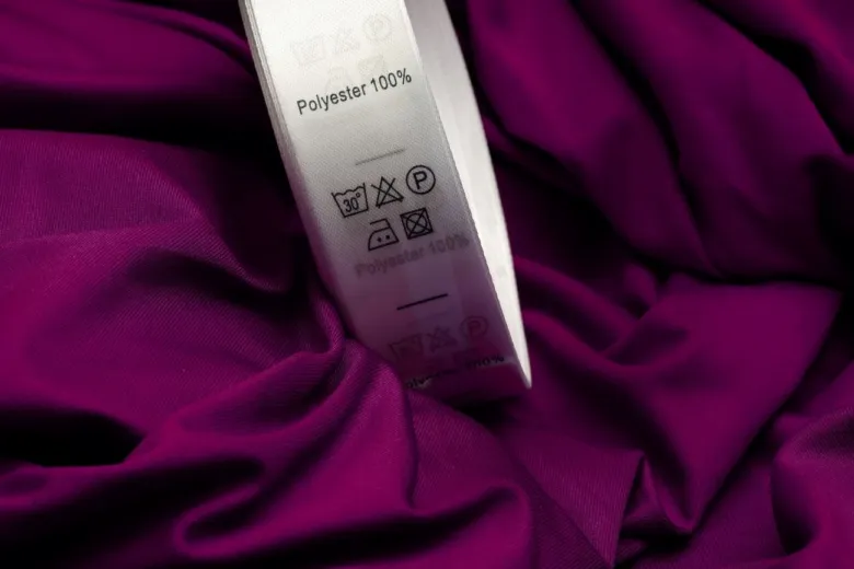Bílá etiketa s nápisem Polyester 100% na fialovém textilu.