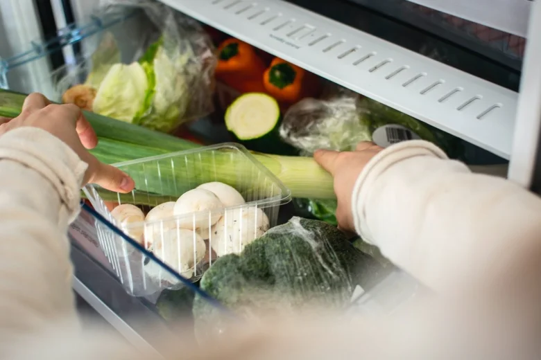 Ruce uspořádávají zeleninu v lednici plné čerstvých produktů.