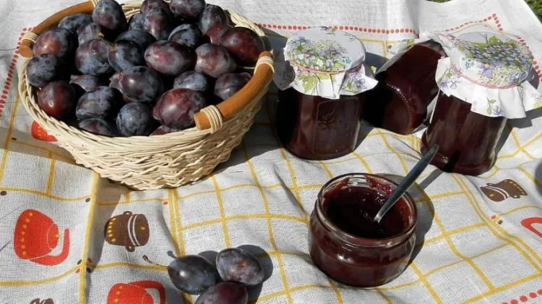 Koš s čerstvými švestkami vedle sklenic domácí marmelády.