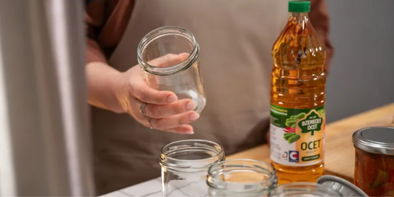 Osoba drží sklenici s víčkem vedle lahve octu pro zavařování.