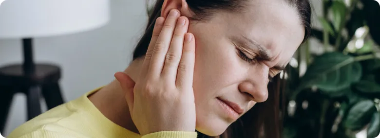 Žena drží ruku u ucha kvůli bolesti nebo zvukovým problémům.