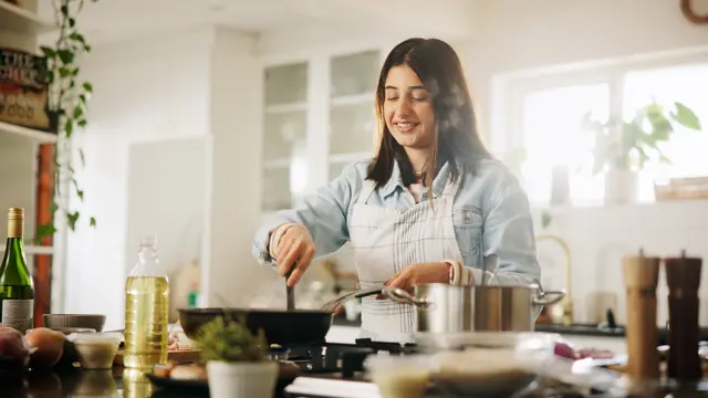 Žena vaří v kuchyni s ingrediencemi na stole.