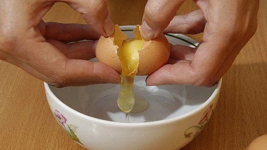 Ruční rozlupování vejce do misky s květinovým vzorem.