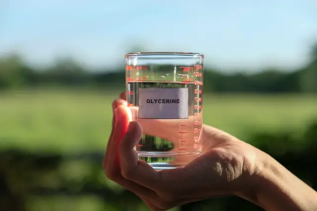 Ruka drží sklenici s glycerinem venku na pozadí zelené přírody.