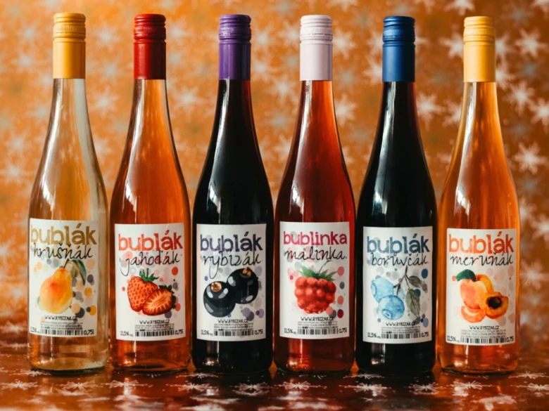 Šest lahví vína s ovocnými štítky na lesklém povrchu.