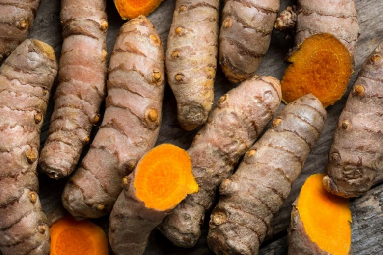 Čerstvé kořeny kurkumu s oranžovým vnitřkem na dřevě.