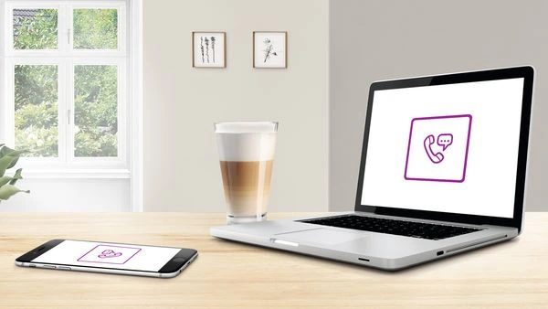 Laptop s ikonou telefonu na stole vedle mobilu u okna.
