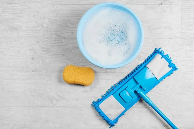 Modrý mop, žlutá houba a miska s pracím prostředkem na podlaze.