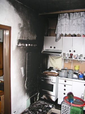 Zapálený kuchyňský interiér po požáru s černým kouřem na stěnách.